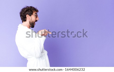 young crazy bearded man  wearing bathrobe against copy space wall