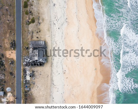 an aerial view of abandoned traditional budu or fish sauce factory near a seaside with waves and sandy beach of terengganu.