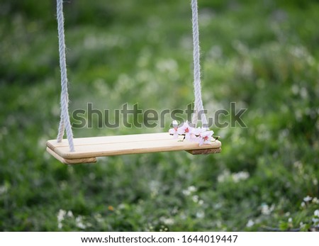 Hanging swings on a background of green grass with flying almonds.