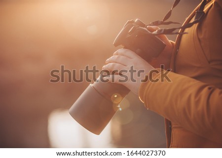 Young woman, photographer holding professional camer in hands during lovely sunset