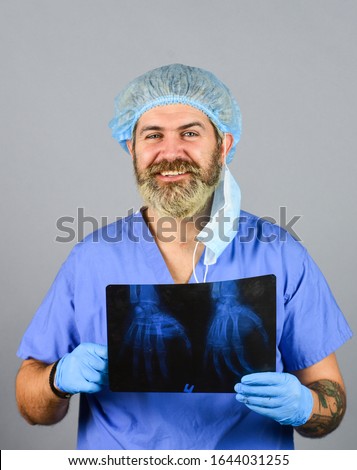 Doctor holds pictures of bones. Fracture and bone damage. Doctor examines radiographic snapshot of wrist. Surgeon estimate damages. Hospital emergency. Doctor compares results. X ray radiation.