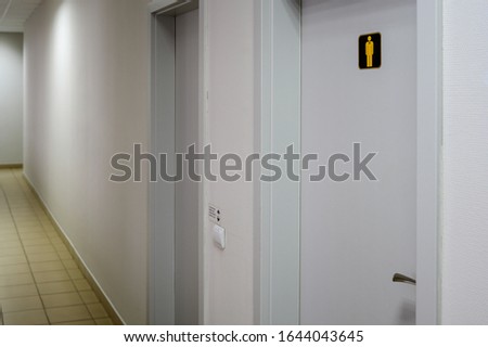 Corridor in the building with doors to the toilet and with white walls.