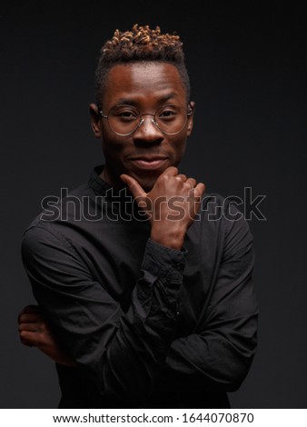 Emotional portrait of a young African man in black clothing against a dark background. Studio photography.