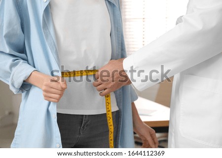 Nutritionist measuring young patient's waist in clinic, closeup