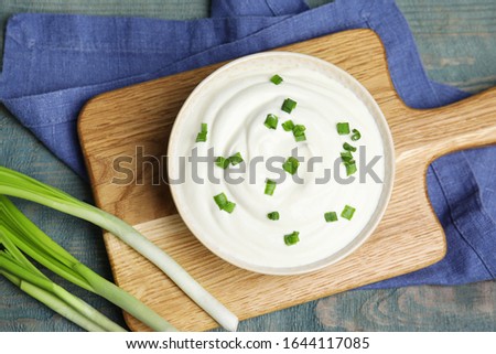 Fresh sour cream with onion on light blue wooden table, flat lay