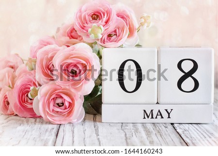 White wood calendar blocks with the date May 8th and pink ranunculus flowers over a wooden table.