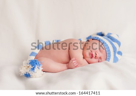 New born baby portrait, lying with hat on head, sleeping