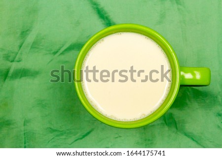Top view of milk in green ceramic cup or mug on green cloth background with copy space. Milk is a high-protein beverage, suitable for everyone. 