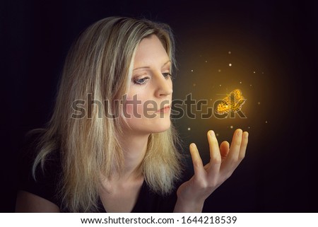 Beauty young blond hair woman hold hand under glowing orange butterfly. Photomanipulation glowing lepidopteran on black background