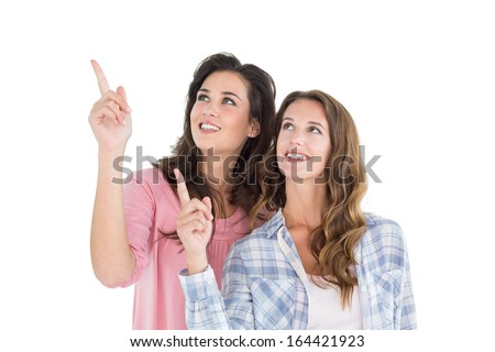 Two young female friends pointing up against white background