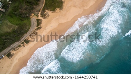 Aerial view of an australian beach with some people walking on it. In the image we can see the waves and a colorful beach with some shadows on it