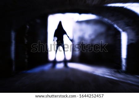 Silhouette of evil theatening body in dark basement - Sinister figure standing at dungeon door with dangerous attitude - Concept of a dreadful encounter with blurred subject in backlight - Image Royalty-Free Stock Photo #1644252457