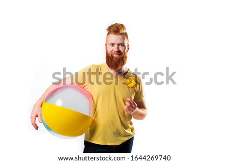 Air ball in hand a young man with glasses with a yellow rim on his face on white isolated.Summer bright yellow photo. Red bearded guy.travel and summer beach vacation concept