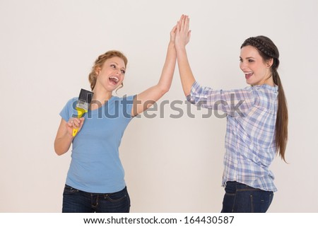 Two cheerful young female friends giving high five against white background
