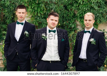 groom and groomsman in suits hold hands in pockets and looking at the camera