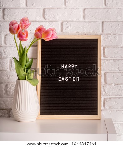 Easter hliday concept. Vase with tulips and black felt letter board with words Happy Easter on white bricks background
