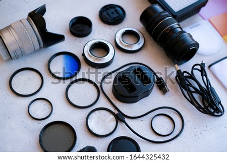 Flat lay composition equipment for professional photographer on grey. Photo gradient filter, macro rings, polarizing filter, charger, video light with color plates, lens caps all for cameras