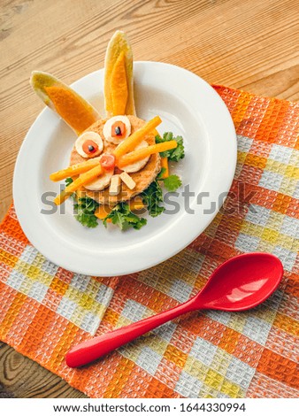 Sandwich made and garnished in the shape of rabbit face to attract children. The sandwich is made of bred slice, papaya, tomato, banana and coriander leaf. It is placed in a white plate.