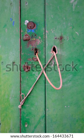 Green door with rusty locks and pink string arrangement.