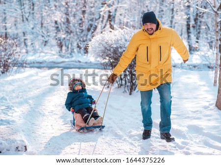 Winter walk: dad sledging with son. Father pulling sled with toddler son in snowy day. Man and child enjoy ride and smile. Focus on face of father. Family fun, happy childhood and activity outdoors