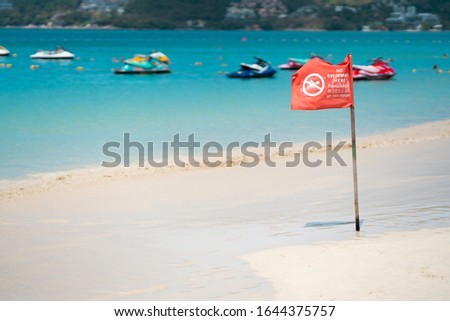 A red flag sign on the beach which is written in 4 languages, English, Thai, Chinese and Russian respectively. All language mean "No swimming here"