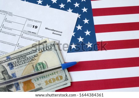 Form 1099-misc Miscellaneous income and blue pen with dollar bills lies on United States flag. Internal revenue service tax form Royalty-Free Stock Photo #1644384361