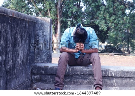 Depressed Teenager man sitting alone on Wall in Outdoor.Unpleasant pain. Sad unhappy handsome man.Bangladeshi and Asia boy Suffering Depression.
