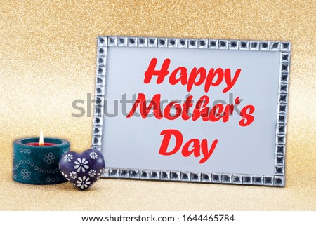 A burning candle, a blue heart and a picture frame with the text HAPPY MOTHER'S DAY