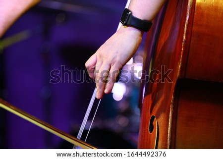 Close-up of hands playing the double bass with a bow.Fragment of an old soundboard of a musical instrument and fingers on strings on a bokeh background.Selective focus.Beautiful art photo