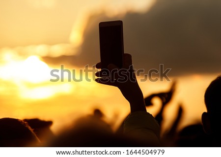 Silhouette of hand using smartphone to take pictures and videos at live music show