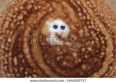 Amazing close up picture about appetizing happy, smiling face on creamy coffee foam on top of a cup of cappuccino in coffee shop; color photo.