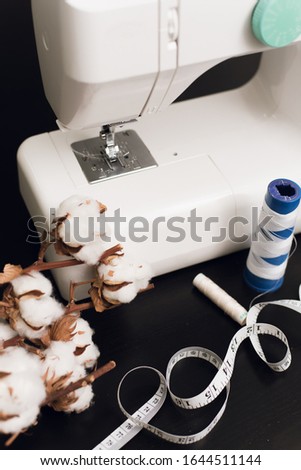 Sewing machine, centimeter, white thread and a branch of cotton flowers on a black background. The concept of sewing, small business, hobby
