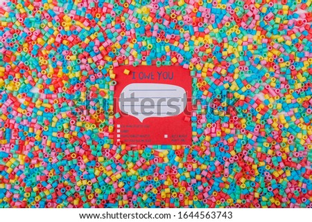 Beautiful greeting card design of text I OWE YOU pinned with a clothes peg in a sea of multicoloured beads.