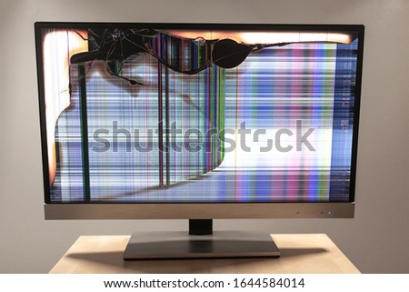 Computer led monitor on a desk with a large crack and colorful lines running across the screen