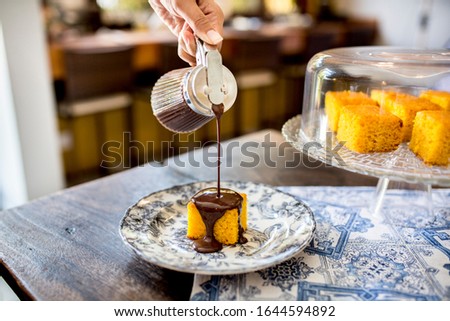 pouring mouth watering melted hot chocolate sauce syrup over a delicious carrot corn fluffy yellow cake on a stylish plate and beautiful table wear over a wooden table