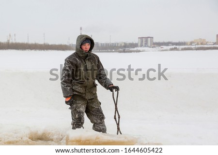 Worker with iron tongs captures on the ice of a frozen river