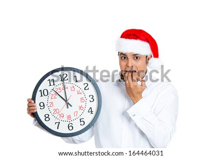 Closeup portrait of worried young man wearing red santa claus hat, hands in mouth holding clock, isolated on white background. Negative emotion facial expression. Last minute christmas shopping