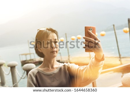 traveling mature Asian woman selfie by mobile phone at Sun Moon Lake, Taiwan