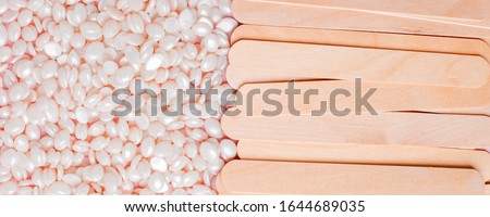 background texture wax for depilation of white pearl color on a pink background with wooden stick spatula. Copy space, banner, flyer, minimal texture. The concept of depilation, waxing, smooth skin 