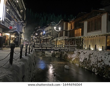 Idyllic Japanese small village new year night winter scenery with traditional houses and wooden bridge with lantern over the river, Ginzan onsen hot spring, Yamagata, Japan