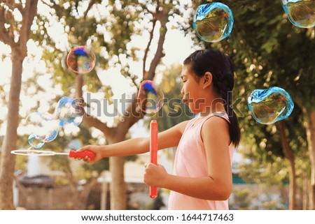 Asian kid in pink dress blowing bubbles in the garden.
