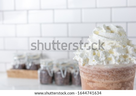A view of an iced coffee beverage with a large swirl of whipped cream in a cafe setting.