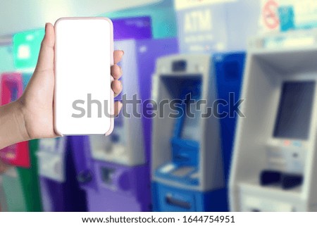 Holding mobile phone on blurry money and atm background. Mobile banking concept.