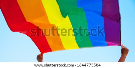 People holding and raising a rainbow flag over the blue sky