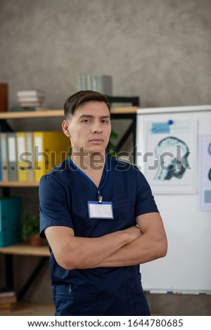 Serious doctor. Young male doctor in dark-blue shirt looking serious