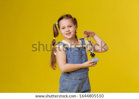 Cute little girl holds a prize. The first hobby is a reward for winning. Participation in the competition. Schoolgirl competes proud of victory. Yellow background studio place for text copyspace