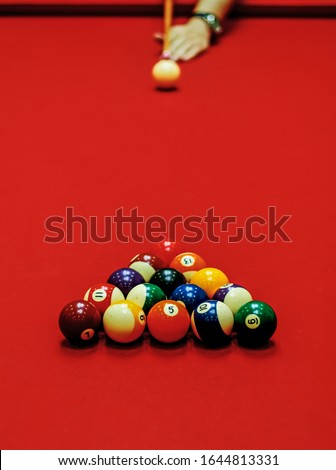 Red billiard table, balls in triangle shape and a hand's shooter with a pool stick  ready to shoot