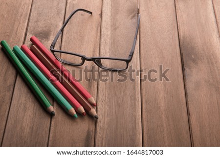 spectacles and color pencils over wooden top with high angle view