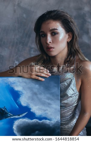 Beautiful woman artist with creative fantasy make up posing with her paintings.