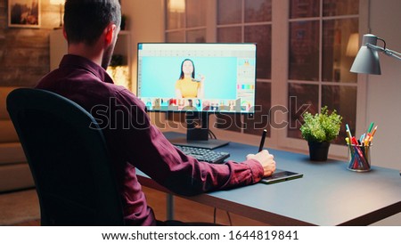 Male photographer editing photos in office at night time using graphic tablet.